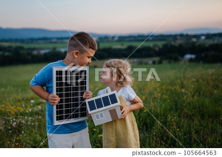 Young boy holding solar panel and his sister holding model of house with installed solar panels. Young boy holding solar panel and his sister holding model of house with installed solar panels. 105664563