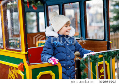 Little preschool girl on a carousel train at Christmas funfair or market, outdoors. Happy child having fun. Traditional xmas market in Germany, Europe. Holiday, children, lifestyle concept Little preschool girl on a carousel train at Christmas funfair or market, outdoors. Happy child having fun. Traditional xmas market in Germany, Europe. Holiday, children, lifestyle concept 105664598