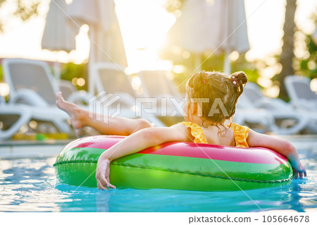 Happy little girl with inflatable toy ring float in swimming pool. Little preschool child learning to swim and dive in outdoor pool of hotel resort. Healthy sport activity and fun for children. Happy little girl with inflatable toy ring float in swimming pool. Little preschool child learning to swim and dive in outdoor pool of hotel resort. Healthy sport activity and fun for children. 105664678