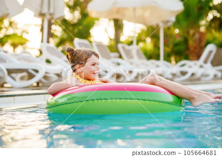 Happy little girl with inflatable toy ring float in swimming pool. Little preschool child learning to swim and dive in outdoor pool of hotel resort. Healthy sport activity and fun for children. 105664681