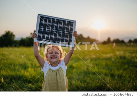 Little girl with model of solar panel, standing in the middle of meadow Concept of renewable resources. 105664683
