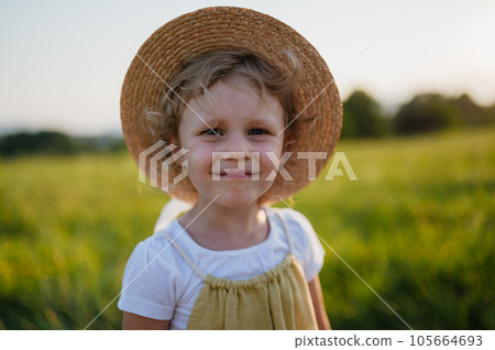 Adorable little girl in a straw hat standing in the middle of summer meadow. Adorable little girl in a straw hat standing in the middle of summer meadow. 105664693
