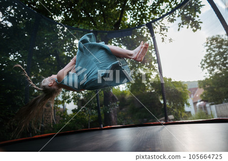 Little girl jumping on trampoline on backyard. Little girl jumping on trampoline on backyard. 105664725