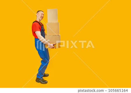 Tired delivery man wear blue uniform workwear and hold big boxes. Courier with cardboard box on yellow background. Copy space, mock up. Tired delivery man wear blue uniform workwear and hold big boxes. Courier with cardboard box on yellow background. Copy space, mock up. 105665164