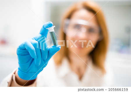 Hand of female scientist in rubber glove shaking test tube with blue reagent, preparing samples for analysis Hand of female scientist in rubber glove shaking test tube with blue reagent, preparing samples for analysis 105666159