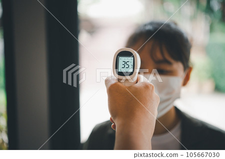 Hand holding infrared thermometer to measuring temperature  people with face mask on background. Covid flu screening 19 concept. 105667030