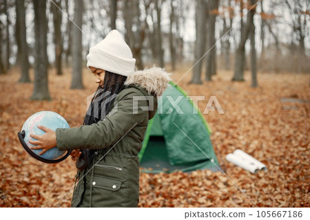 One little black girl in tent camping in the forest. Girl is holding a globe in her hands. Black girl wearing khaki coat and beige hat. One little black girl in tent camping in the forest. Girl is holding a globe in her hands. Black girl wearing khaki coat and beige hat. 105667186