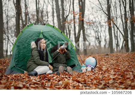 Beautiful little black girls in tent camping in the forest. Two little sisters sitting in a tent in autumn forest and looking on a globe. Black girls wearing khaki coats. 105667206
