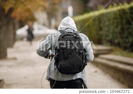Man carry black backpack and walking on the street. Man wearing grey shirt and white hoodie. Back side photo of a man on the street. 105667272