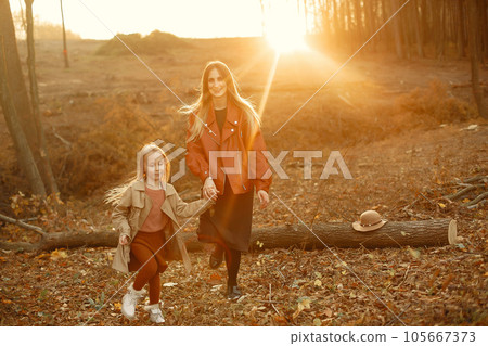 Fashionable mother with daughter. Family in a autumn park. Little daughter in a brown coat. 105667373