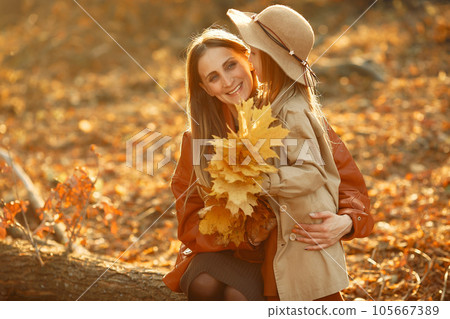 Fashionable mother with daughter. Family in a autumn park. Little daughter in a brown coat. 105667389