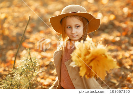 Cute child in a autumn park. Elegant little lady with blonde hair. Girl in a brown coat. Cute child in a autumn park. Elegant little lady with blonde hair. Girl in a brown coat. 105667390
