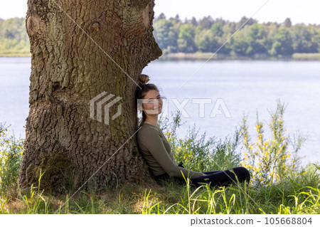 Enchanted Dreams: Young Woman Gazing at the Forest Lake from Beneath a Tree 105668804