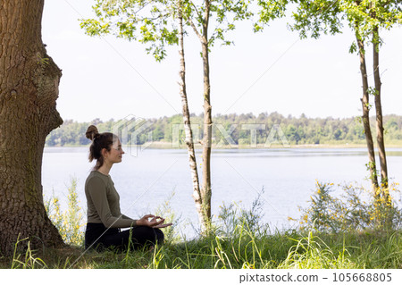 Serenity in Nature: Young Woman Meditating by the Forest Lake 105668805