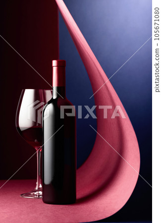 Bottle and glass of red wine on a red-blue background. 105671080