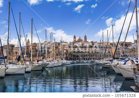 Senglea, Malta waterfront with moored leisure boats and traditional limestone buildings with balconies against blue sky with clouds. Senglea, Malta waterfront with moored leisure boats and traditional limestone buildings with balconies against blue sky with clouds. 105671328