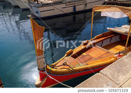 Dghaisa tal-pass with distinctive fore stempost, traditional Maltese water taxi boat without crowd moored on the waterfront of Birgu, Malta. Dghaisa tal-pass with distinctive fore stempost, traditional Maltese water taxi boat without crowd moored on the waterfront of Birgu, Malta. 105671329