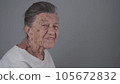 Senior woman 90 years old smiles, laughs and shows a denture on a gray background. Elderly female with deep wrinkles and gray hair happy in a good mood studio portrait looking at camera 105672832
