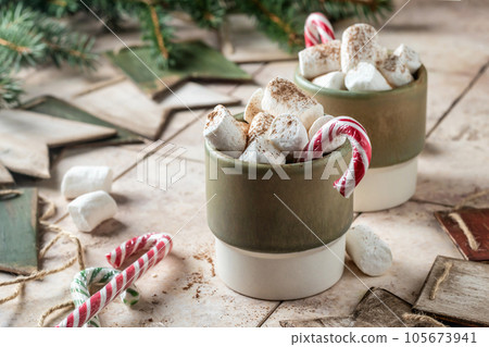 Holiday xmas food mug with hot chocolate cocoa and marshmallows decorated with candy canes with fir xmas tree branches on beige tile background. Christmas festive card 105673941