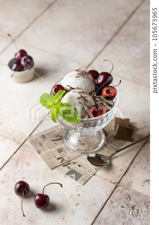 Ice cream in balls with cherry, chocolate and mint in glass bowl on beige tile background, summer refreshing morning dessert, vertical Ice cream in balls with cherry, chocolate and mint in glass bowl on beige tile background, summer refreshing morning dessert, vertical 105673965