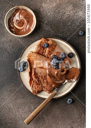 Chocolate Crepes with blueberry and chocolate paste on brown textured background rustic style top view, flat lay Chocolate Crepes with blueberry and chocolate paste on brown textured background rustic style top view, flat lay 105673986