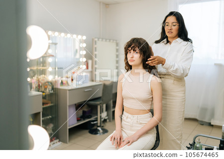 Portrait of young beautiful woman having hair cut at female hairstylist in modern beauty studio. Pretty lady looking at camera in hairdresser saloon having haircut. Concept of fashion and beauty. Portrait of young beautiful woman having hair cut at female hairstylist in modern beauty studio. Pretty lady looking at camera in hairdresser saloon having haircut. Concept of fashion and beauty. 105674465