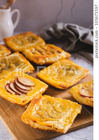 Small upside-down puff pastry tarts with apple and banana on the board vertical view Small upside-down puff pastry tarts with apple and banana on the board vertical view 105675597