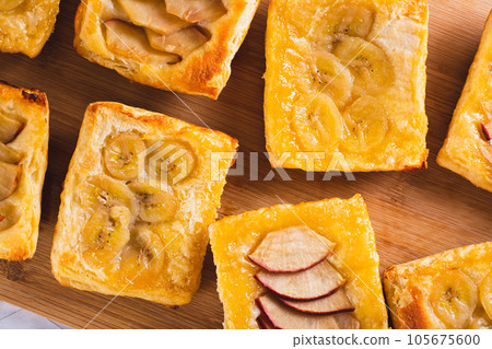 Close up of upside-down puff pastry tarts with apple and banana on the board top view Close up of upside-down puff pastry tarts with apple and banana on the board top view 105675600