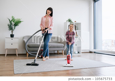 Lady and girl standing with cleaning devices in living room Lady and girl standing with cleaning devices in living room 105675733