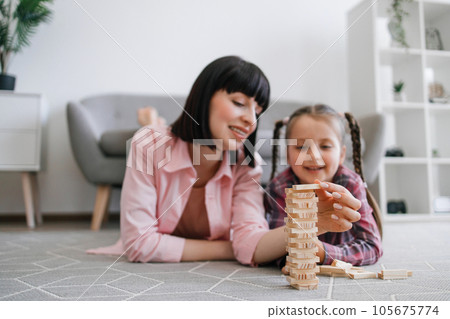 Woman and tween girl enjoying tower building game on carpet Woman and tween girl enjoying tower building game on carpet 105675774