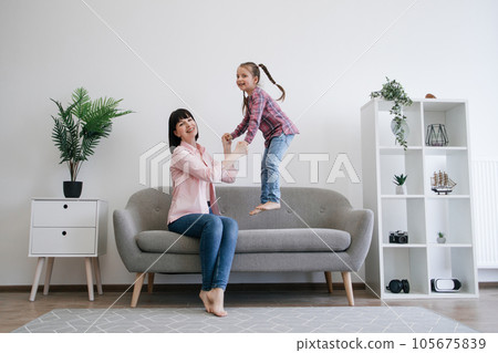 Mom-daughter duo testing bounce of couch in family lounge Mom-daughter duo testing bounce of couch in family lounge 105675839