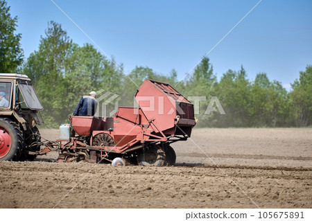 Farmland during planting of potatoes with potato planter hitched to tractor. Farmland during planting of potatoes with potato planter hitched to tractor. 105675891
