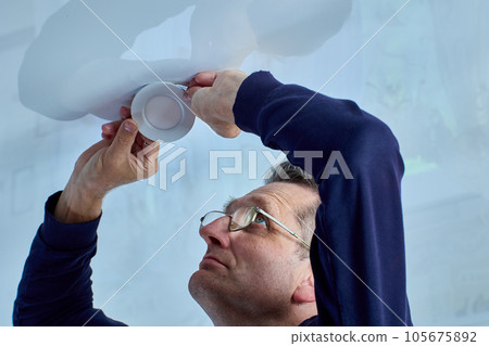 LED spotlight is being repaired by an elderly repairman, electrician removed lighting fixture from socket in ceiling. LED spotlight is being repaired by an elderly repairman, electrician removed lighting fixture from socket in ceiling. 105675892