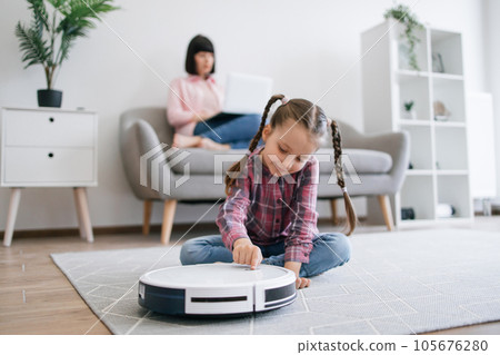 Child activating robot vacuum while mom doing online job Child activating robot vacuum while mom doing online job 105676280
