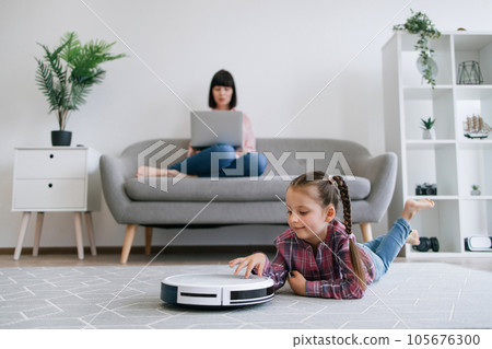 Kid watching robot vacuum cleaning when mom doing remote job Kid watching robot vacuum cleaning when mom doing remote job 105676300