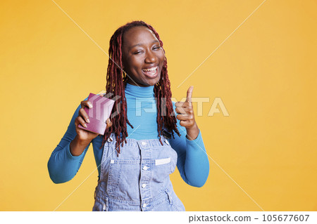 Young traveller doing like sign holding passport before leaving on vacation trip, being excited about international citybreak. Cheerful modern girl travelling on urban destination with id pass. Young traveller doing like sign holding passport before leaving on vacation trip, being excited about international citybreak. Cheerful modern girl travelling on urban destination with id pass. 105677607