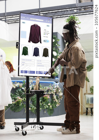Shopper looks for clothes on monitor kiosk service in fashion boutique at mall. Male customer shopping for clothing line items in retail store, touch screen board for self service concept. 105677624
