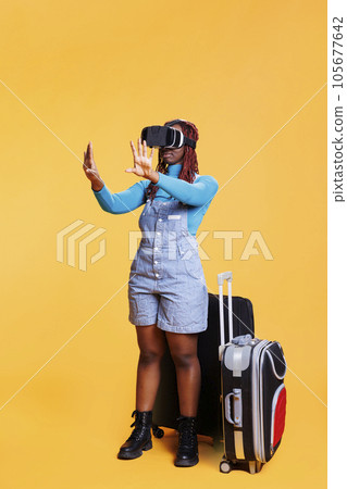 Modern girl using vr headset on holiday, carrying suitcase bags and using virtual reality glasses. Young tourist having fun with artificial intelligence 3d goggles, travelling on vacation. 105677642