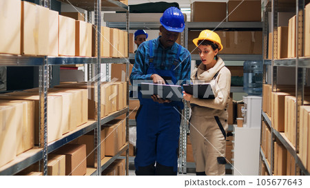 Multiethnic team of employees working with goods and checking stock inventory on laptop, cargo in storage room. Depot workers analyzing industrial goods to plan distribution and shipment. 105677643