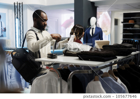 Customer examining tie and shirt match while shopping in clothing store. African american man choosing formal apparel and accessory, checking garment size and style in showroom 105677646
