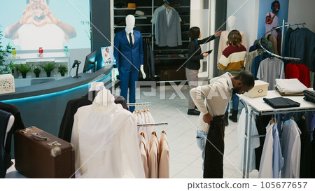 Multiethnic group of people looking at trendy clothes in retail store market, shopping for formal or casual wear. Diverse customers examining fashion collections on hangers, commercial activity. Multiethnic group of people looking at trendy clothes in retail store market, shopping for formal or casual wear. Diverse customers examining fashion collections on hangers, commercial activity. 105677657