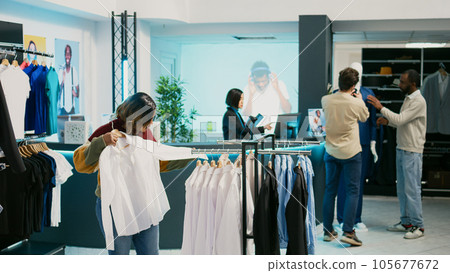 Female customer looking at merchandise in clothing store, shopping for new trendy collection. Young woman checking clothes hanging in department store, modern fashion boutique. 105677672