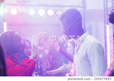 African american couple showing hands moves while improvising dance battle in dark nightclub illuminated with lights. Young dancers partying at discotheque in crowded club 105677693