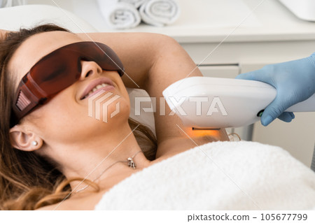 Immersed in an atmosphere of calm, a woman trusts a beautician by visiting the photoepilation procedure in a beauty salon. Beauty support and skin care. In red goggles. Immersed in an atmosphere of calm, a woman trusts a beautician by visiting the photoepilation procedure in a beauty salon. Beauty support and skin care. In red goggles. 105677799