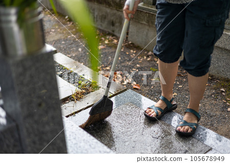 The feet of a woman who is cleaning with a broom after visiting a grave 105678949