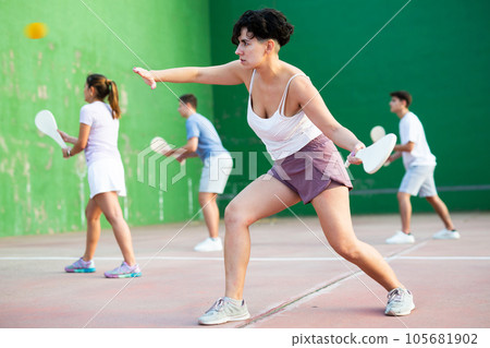 Active womans with enthusiasm playing paleta fronton group on outdoor court 105681902