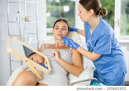 Woman cosmetologist examines patients nasolabial area after lifting procedure and palpates lips mouth 105681933