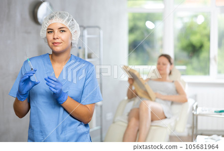 Nurse in disposable cap with syringe in hand and conducts preparatory activities before injections. 105681964