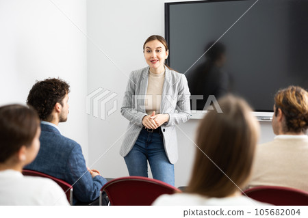 Young woman standing near interactive board and communicating with adult students during advanced training courses in classroom 105682004