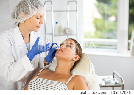 Adult woman cosmetologist makes injection in lips of patient 105682026